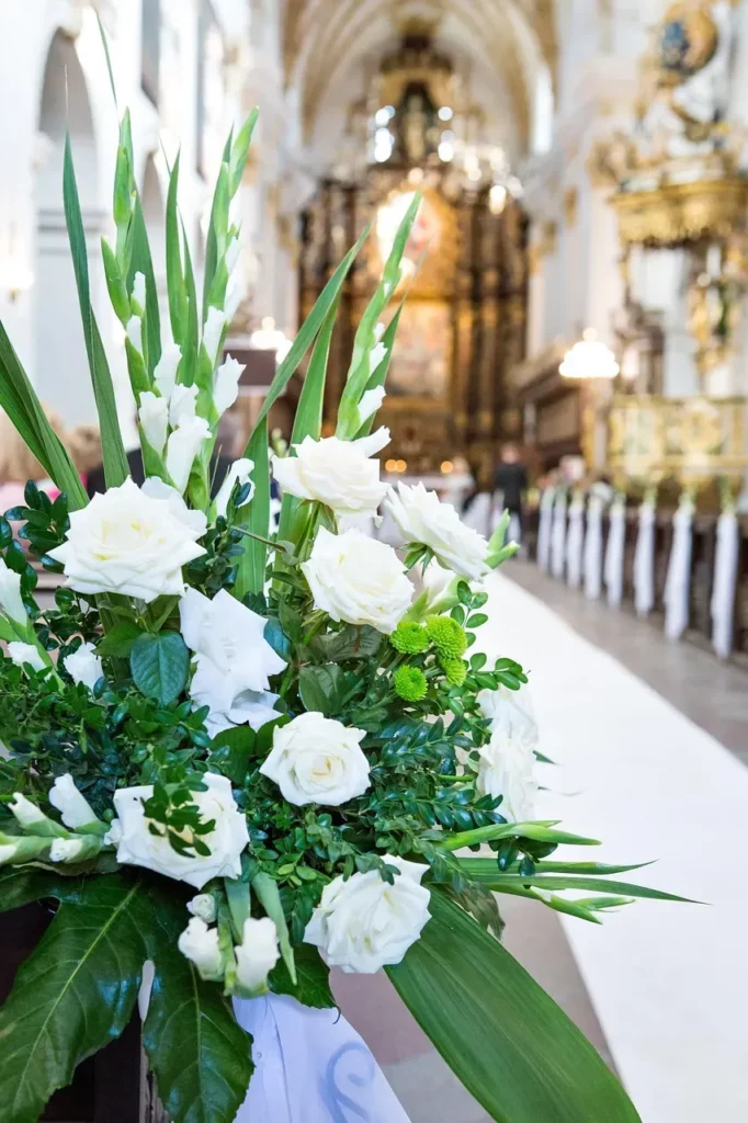 Composition florale de lys et de roses blanches disposée dans l'allée centrale d'une église