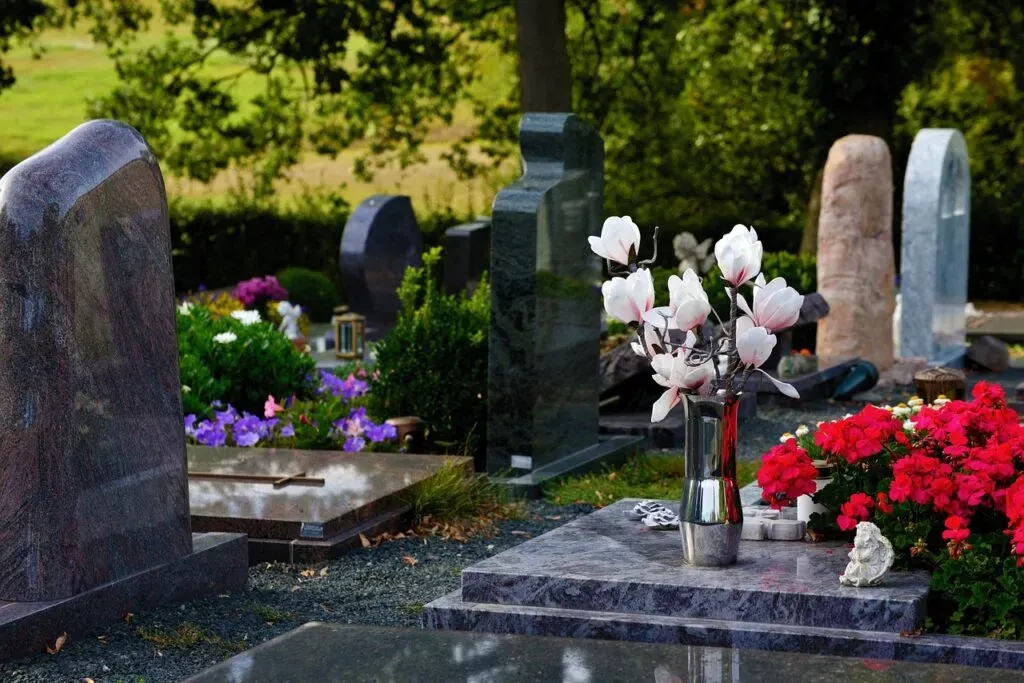 Monuments funéraires en granit décorés de fleurs fraîches et d'un vase dans un cimetière paysager