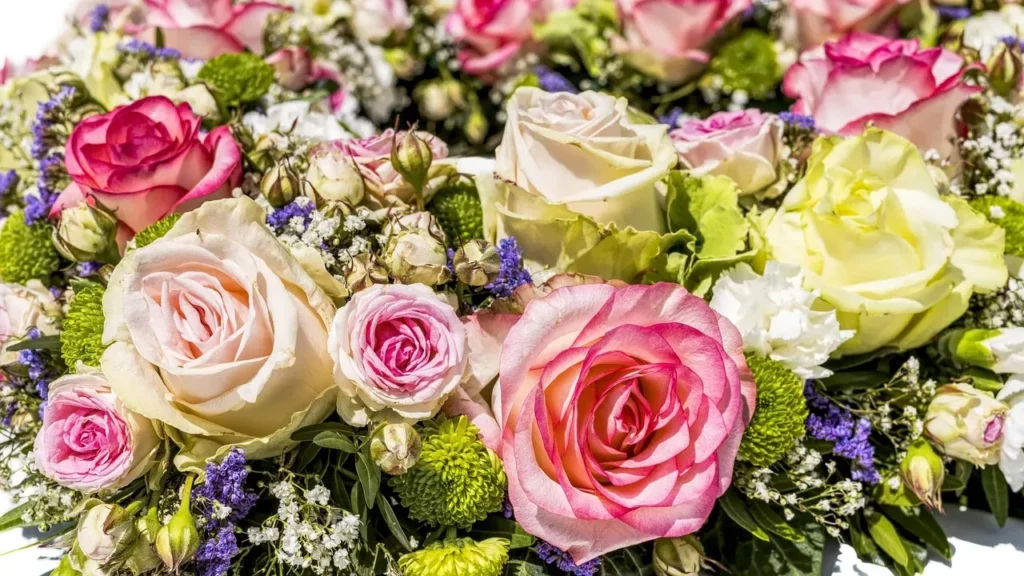 Composition florale de deuil colorée avec roses roses, blanches et touches de fleurs violettes